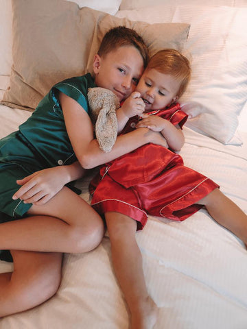 little boy and little girl in red and green chrismas pjs cuddling on bed