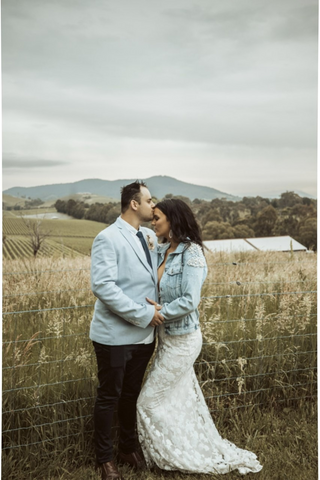 bride and groom hugging in country setting wearing bride pearl denim jacket