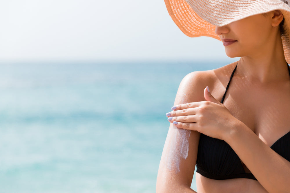 woman at beach applying sunscreen to arm