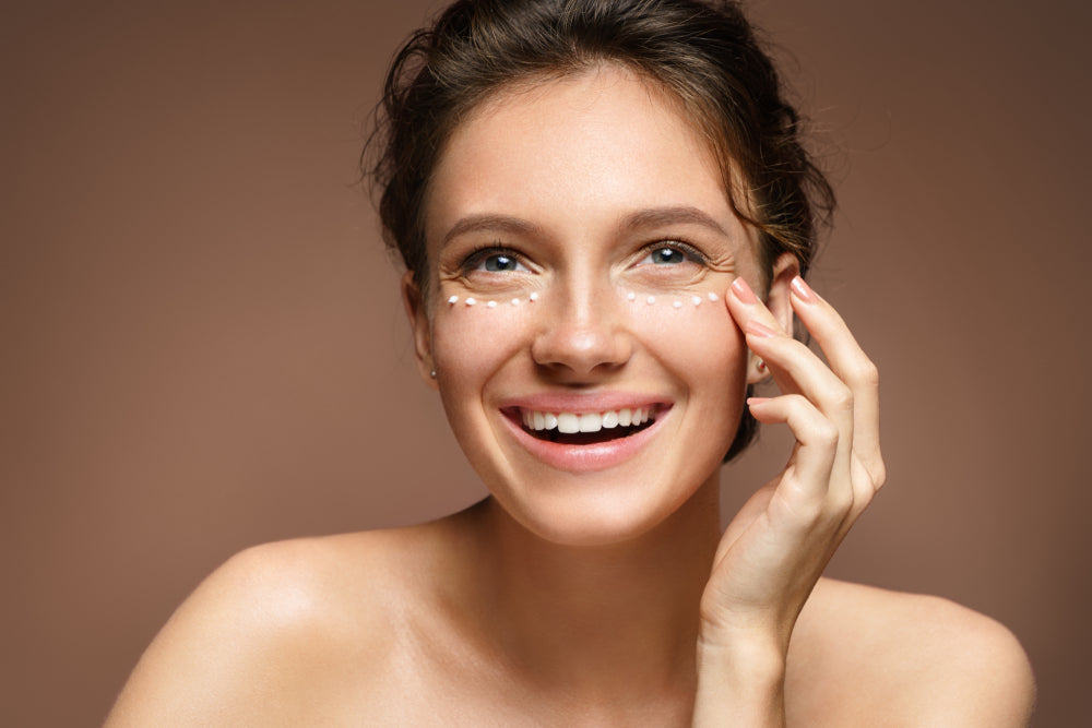 Woman applying eye cream under her eyes and smiling.