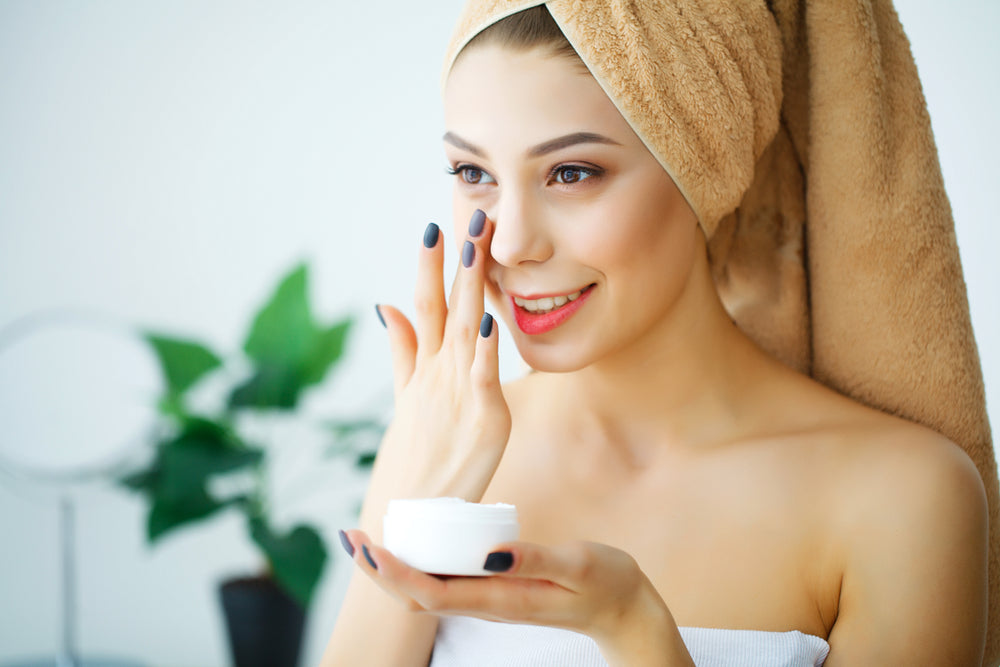 Woman with hair in towel applying skin care cream to her face