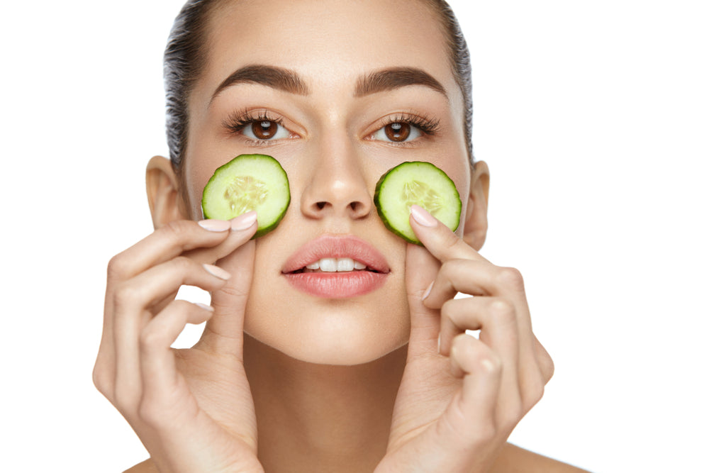 woman putting cucumber slices on each of her cheeks to get rid of dark circles under eyes