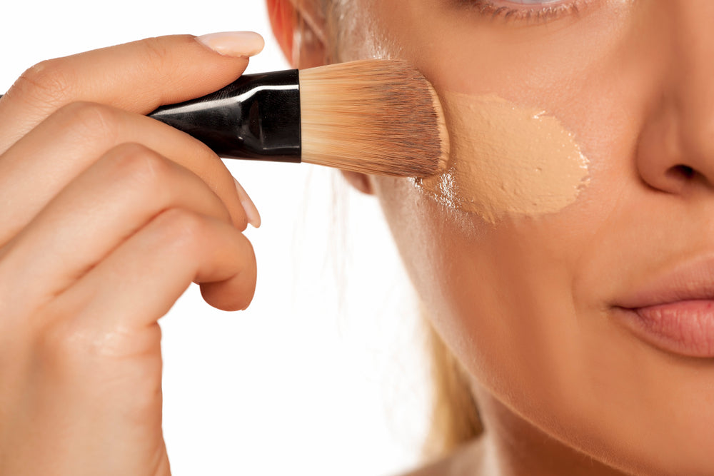 Close-up of a woman applying foundation to her cheek with a brush.