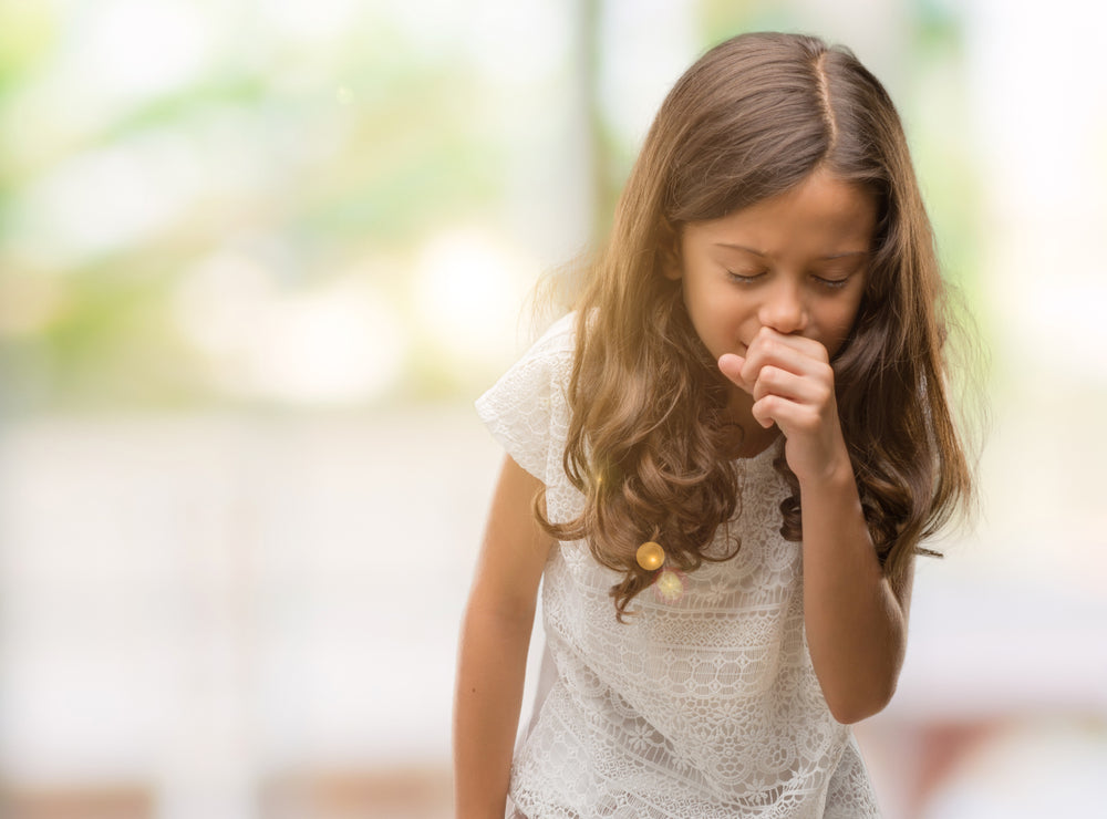 Little girl coughing into her hand.