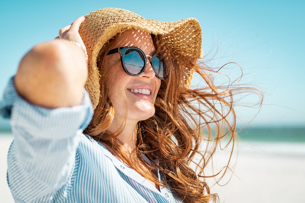 Woman at beach wearing zinc oxide sunscreen, sunglasses, and a sun hat.