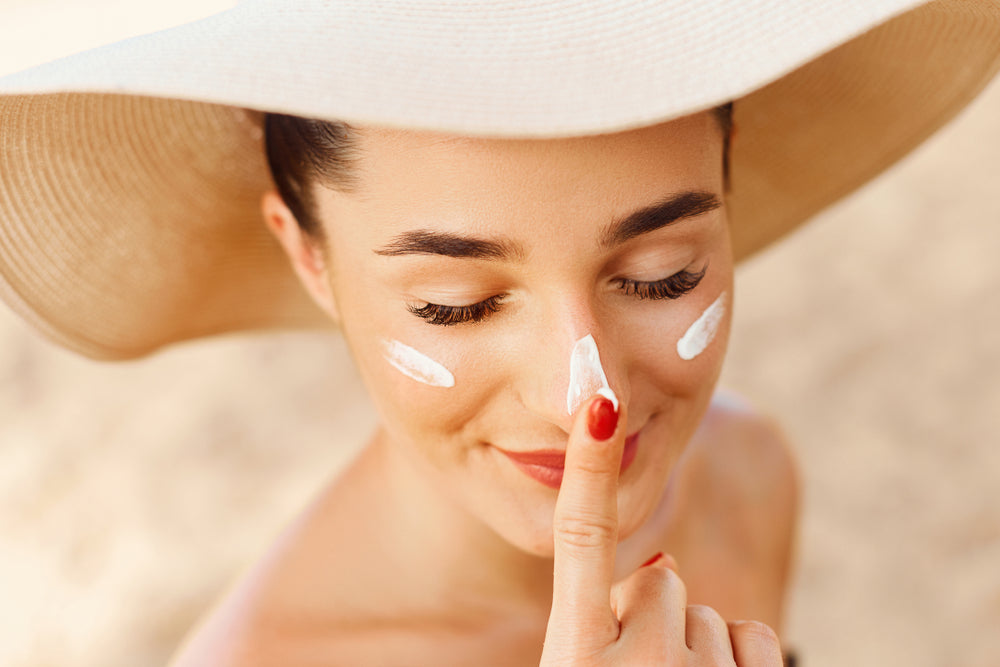 Woman in tan sun hat applying sunscreen to her face