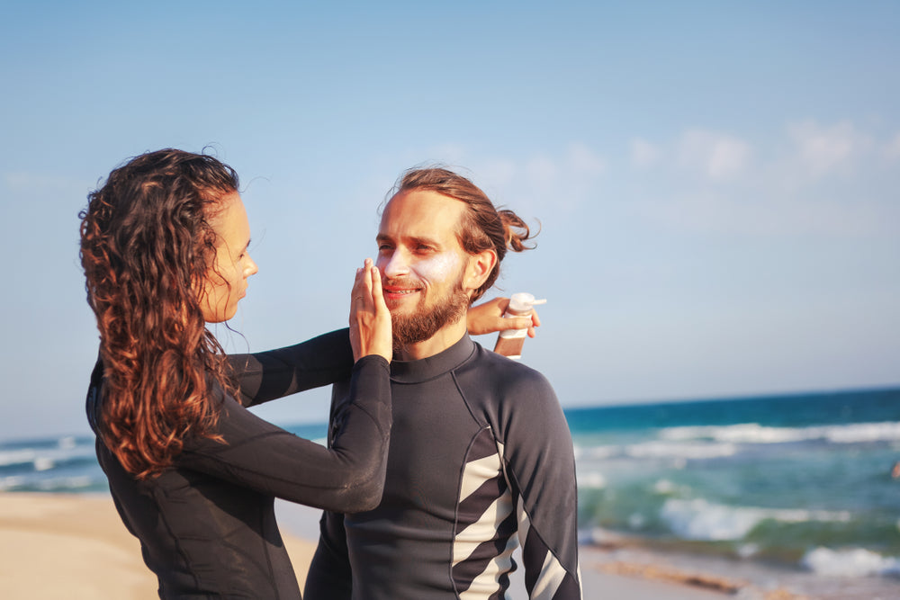 Woman applying sunscreen on man's face at the beach