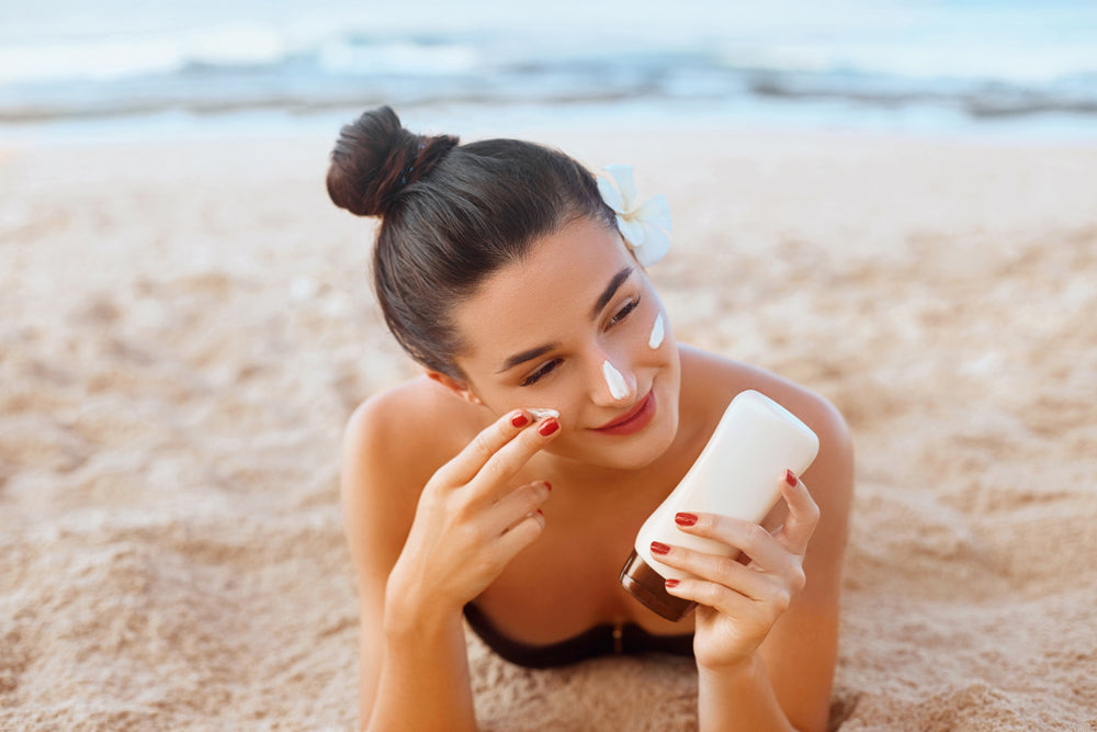 Image of woman laying on beach and applying sunscreen on her face.