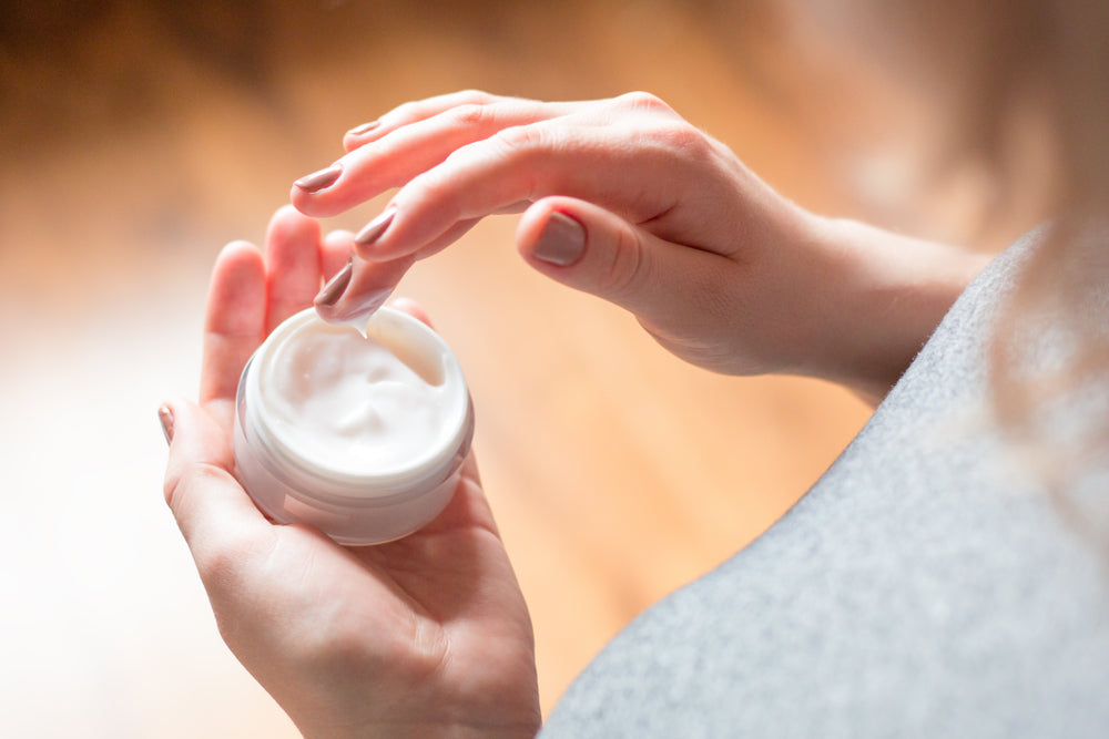 Woman dipping her fingers into a face moisturizer container.