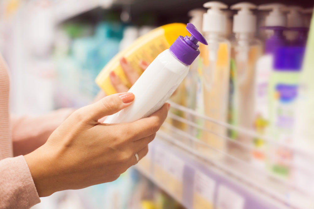 Close-up of woman holding two sunscreen bottles and looking at ingredients in the aisle of a store.