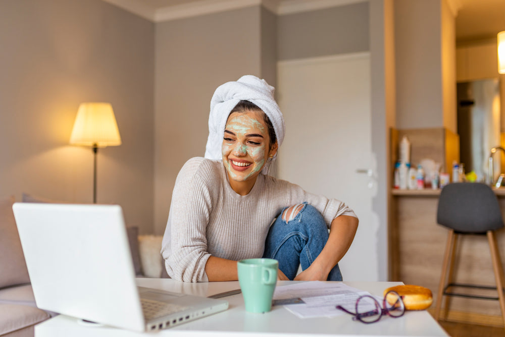 Woman smiling at laptop on table with face redness treating product on her face