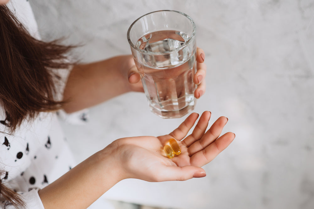 Woman holding Vitamin D supplements in one hand and glass of water in the other 