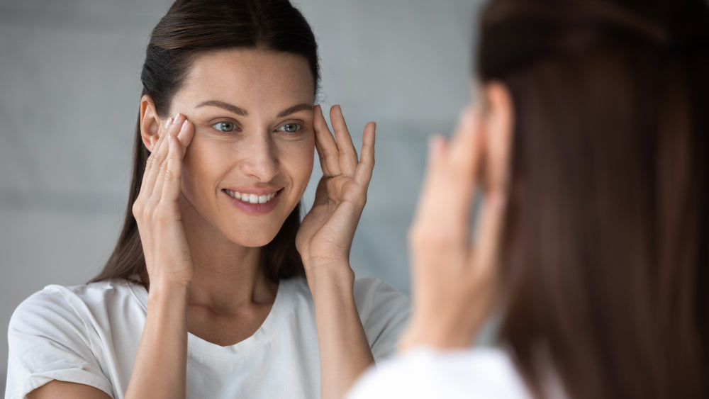 Woman looking at herself in the mirror with her hands at the side of her eyes.