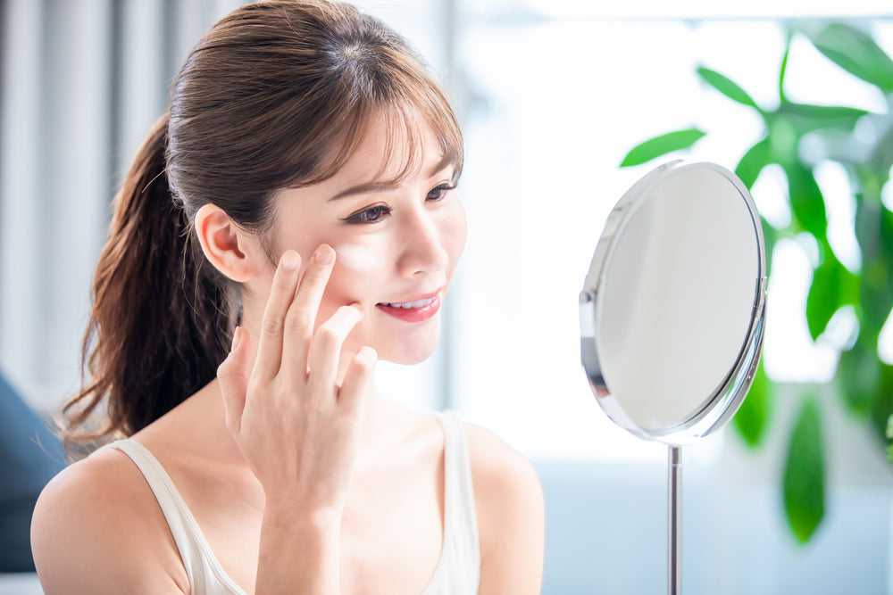 Woman reapplying sunscreen over makeup while looking in the mirror