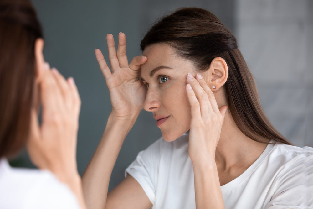 Woman pulling face wrinkles taut while looking in the mirror.