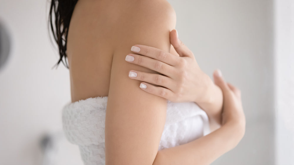 Close up of a woman wrapped in a towel touching her own arm.