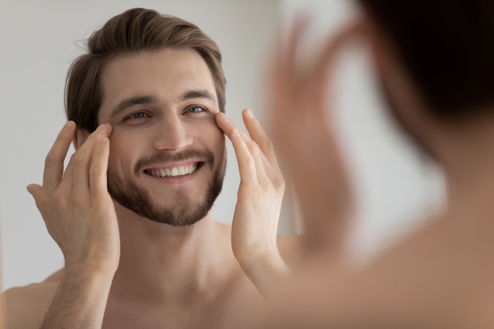 Man looking at under-eye wrinkles while smiling and looking in the mirror