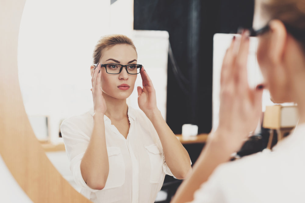 Woman wearing glasses checking her makeup in a mirror