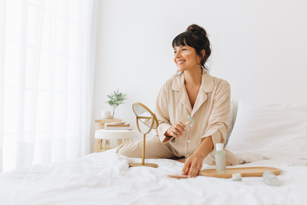 Image of a woman sitting on her bed doing her skincare routine.