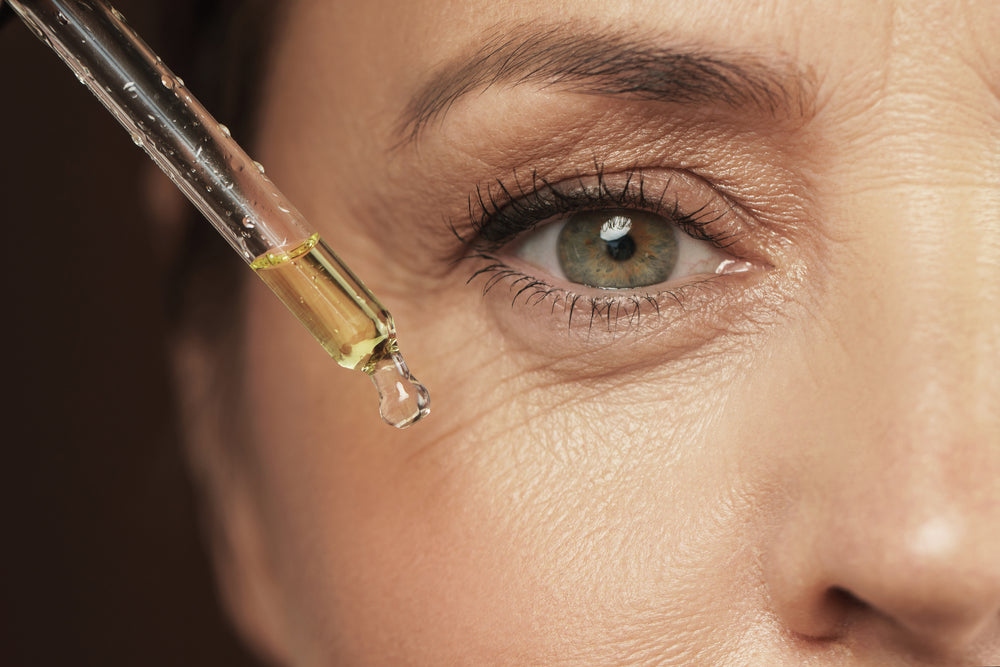 Close up of woman’s eye with wrinkles and her applying a dropper of antioxidant serum to the area.