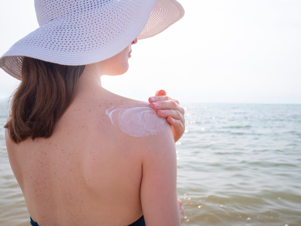 woman in white sun hat using waterproof sunscreen on her shoulder to avoid the need for home remedies for sunburn skin