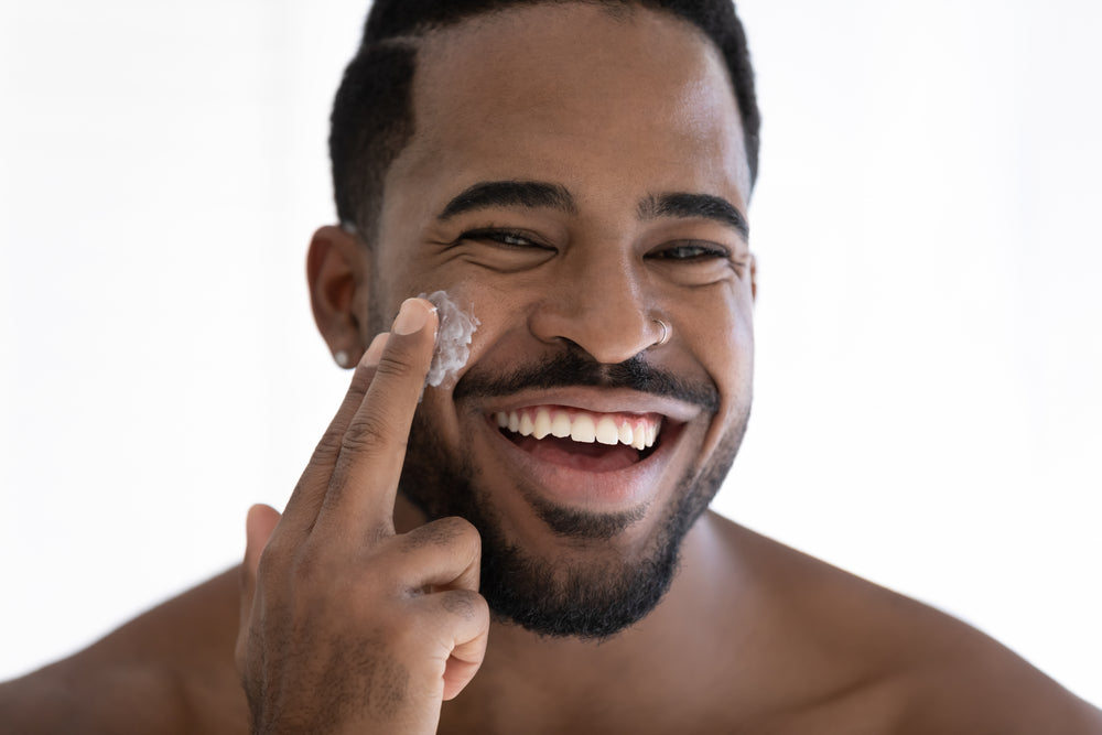 Young Black man applying sunscreen to his face.