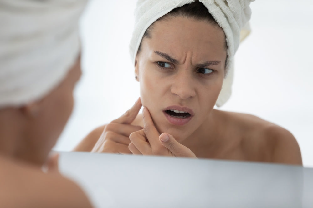 Woman looking in mirror at acne on face