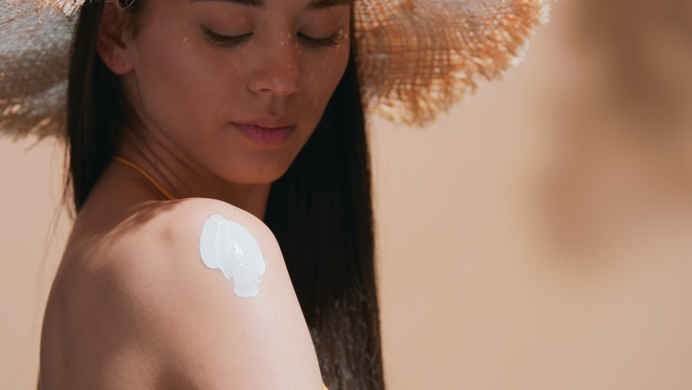 Image of Asian woman wearing a straw hat with sunscreen on her shoulder.