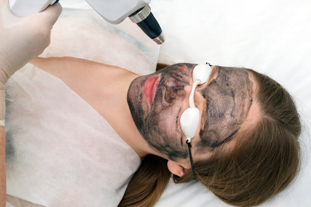 Woman wearing goggles and laying on treatment table while undergoing laser treatment on her face.
