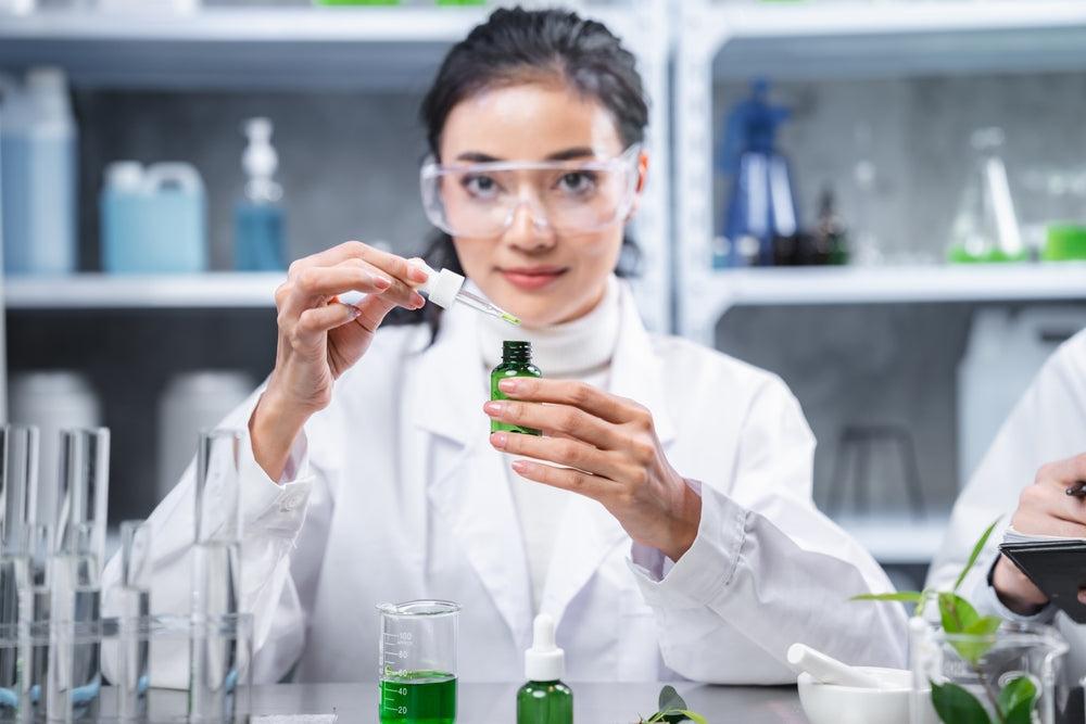 Young Asian woman in a lab coat mixing skincare ingredients.