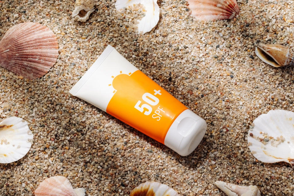Image of a bottle of sunscreen with an SPF 50+ label sitting on the sand.