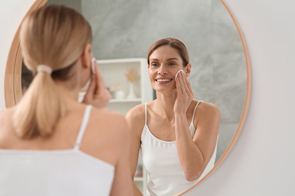 Woman removing makeup from skin while looking at herschel in the mirror