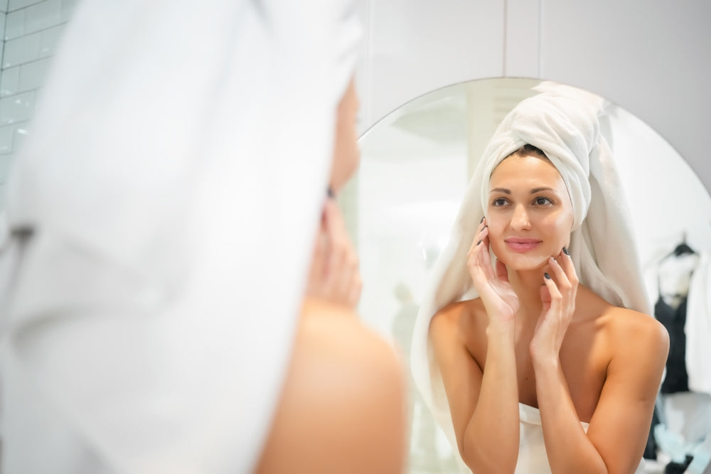 Woman with well-hydrated skin looking at herself in the bathroom mirror.