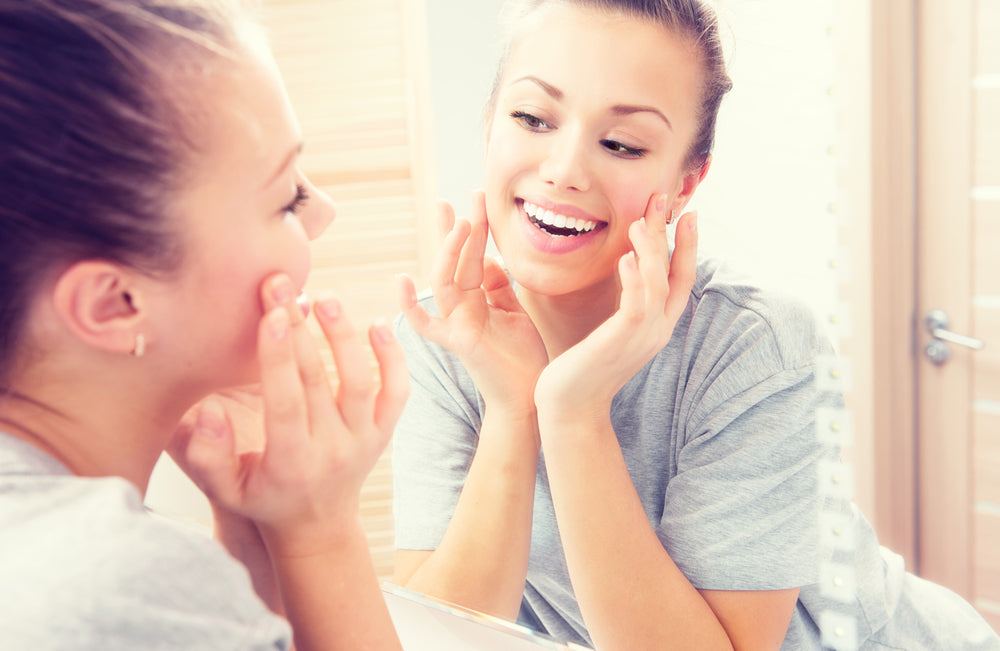  White teen girl touching her face and smiling in the mirror.