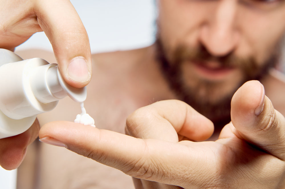 Close up of man putting face lotion on his finger that will protect his skin barrier.