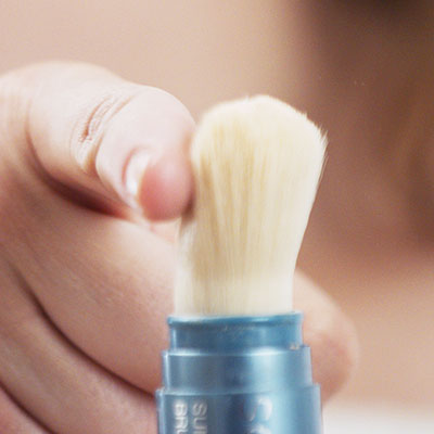 hand flicking the Sunforgettable® Total Protection™ Brush-on Shield SPF50 on the table