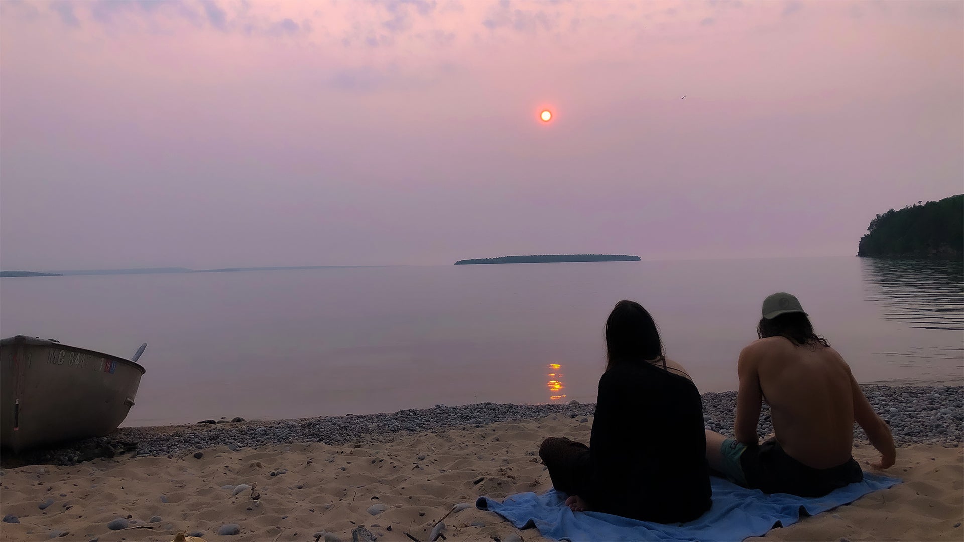 Photo of Couple Sitting on the Beach in Grand Island, Michigan wearing MuskOx Apparel Logo Hat