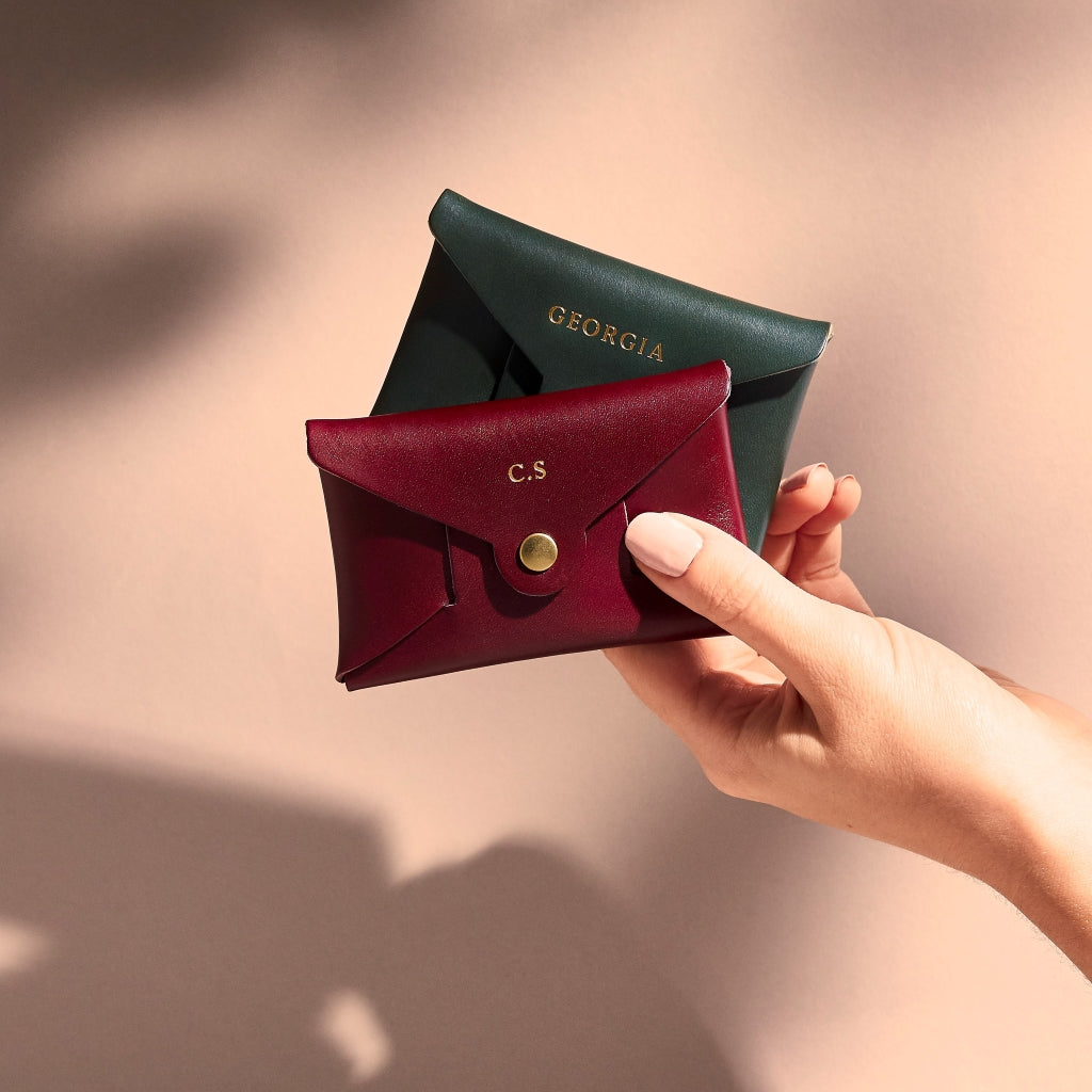 A pair of personalised leather coin purses from Sbri in burgundy and forest green, photographed in hand