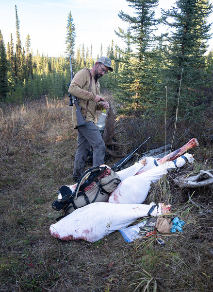 A man stands over a quartered moose in game bags