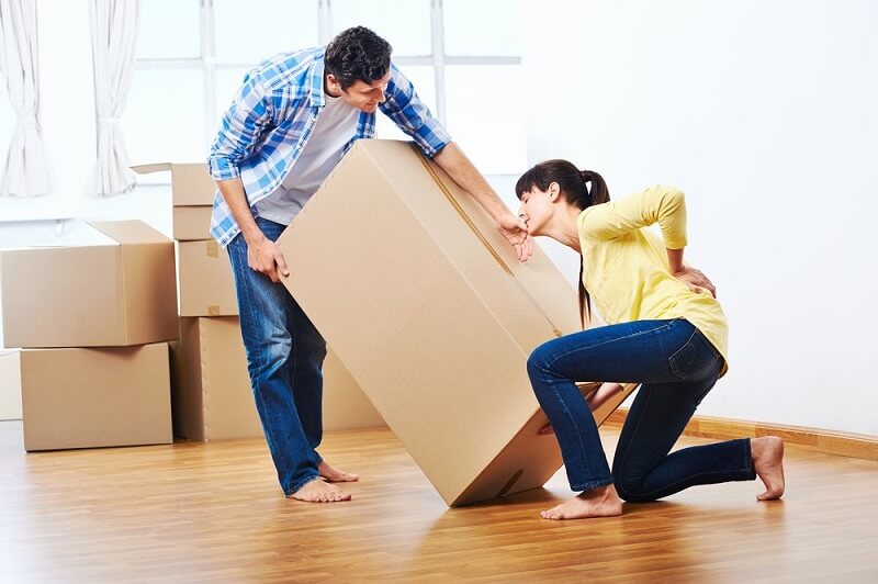 Image of a couple lifting a heavy box with the lady clutching her back in pain.