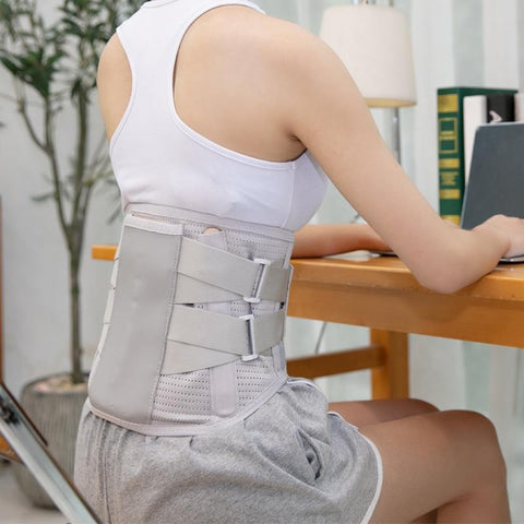 Image of a woman working on a laptop while wearing the OrthoRelieve LumbarMate back brace.