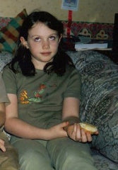 Eilidh as a child wearing a green t shirt and trousers.  They are rolling their eyes.