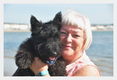 Hilary is pictured with water in the background holding up her black dog