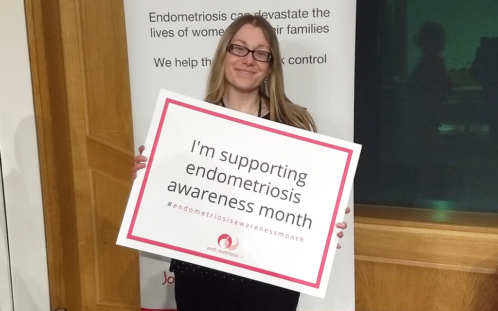 Vicky is standing holding a sign that says "I'm supporting endometriosis awareness month." With the Endometriosis UK logo at the bottom. She is smiling to camera.