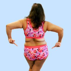 Model is standing with her back to camera and pointing at her bum. She is wearing a flamingo print underwear set.