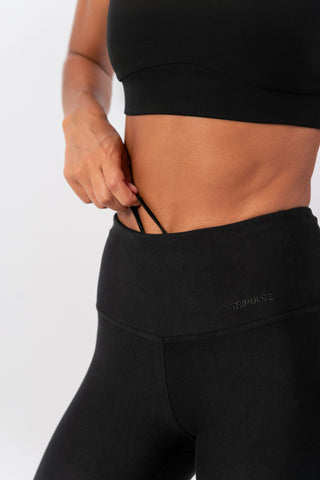 Close-up of woman wearing Tripulse Original Leggings waistband in black pulling hidden drawstring.