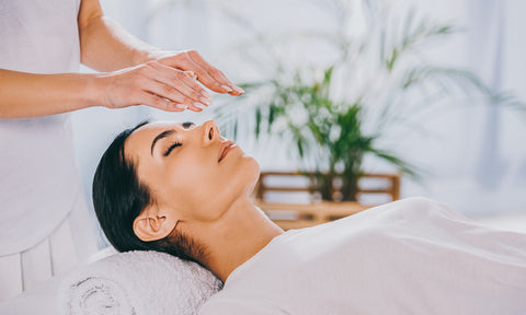 Woman laying down with a Reiki practitioner's hands hovering over her forehead or third eye.