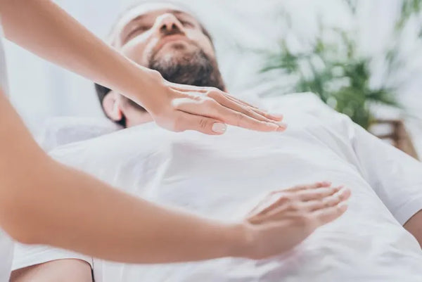 Man laying down with a Reiki Practitioner's hands overing over his heart charkra and solor plexus.