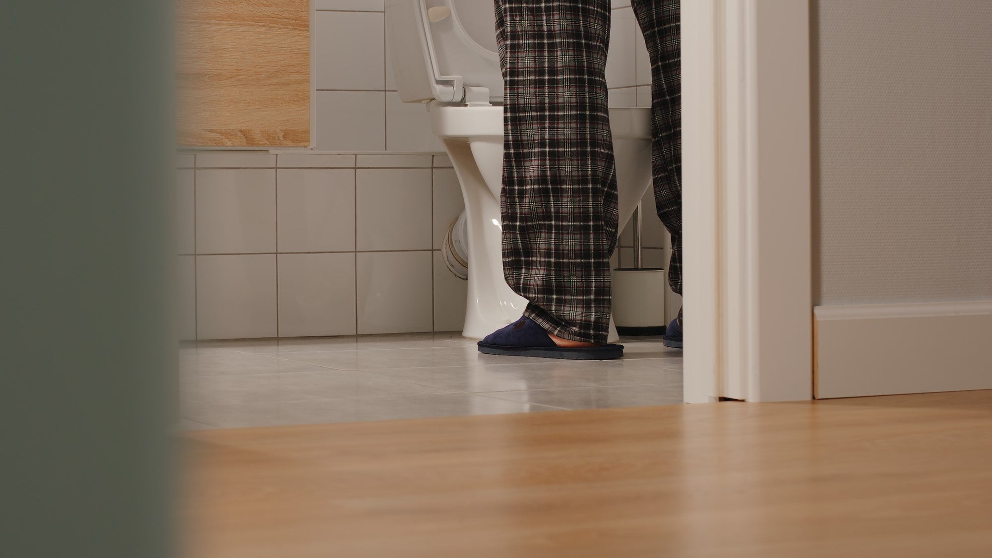 man in pyjamas and slippers standing at toilet, only lower legs visible