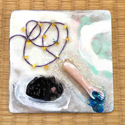 Square painting with doll arm, glitter puddle, and tiny gold stars on a purple thread by Alex Mitchell.